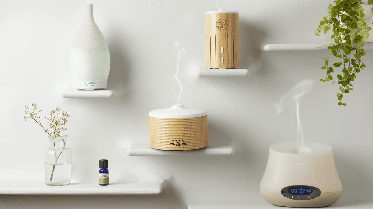 Different Neal's Yard Remedies Diffusers sit on shelving with plants and essential oils