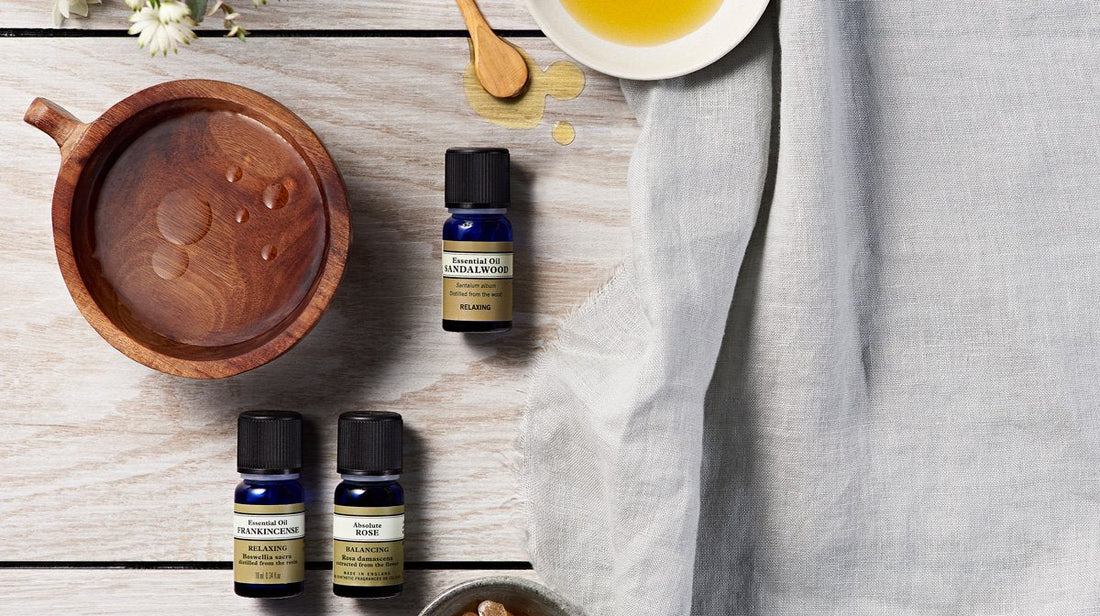 Essential oil bottles besides a wooden bowl containing drops of oil