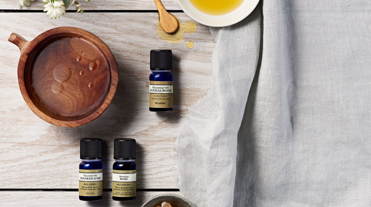 Essential oil bottles besides a wooden bowl containing drops of oil