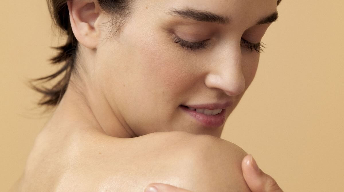 close up of a woman massaging in a product, she is smiling at the camera with her body turned away