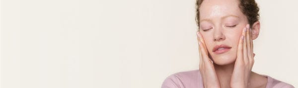Woman with closed eyes touching her face against a light pink background