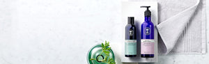 Picture of a shower gel and a body lotion a grey towel and plant in vase by Neal's Yard Remedies