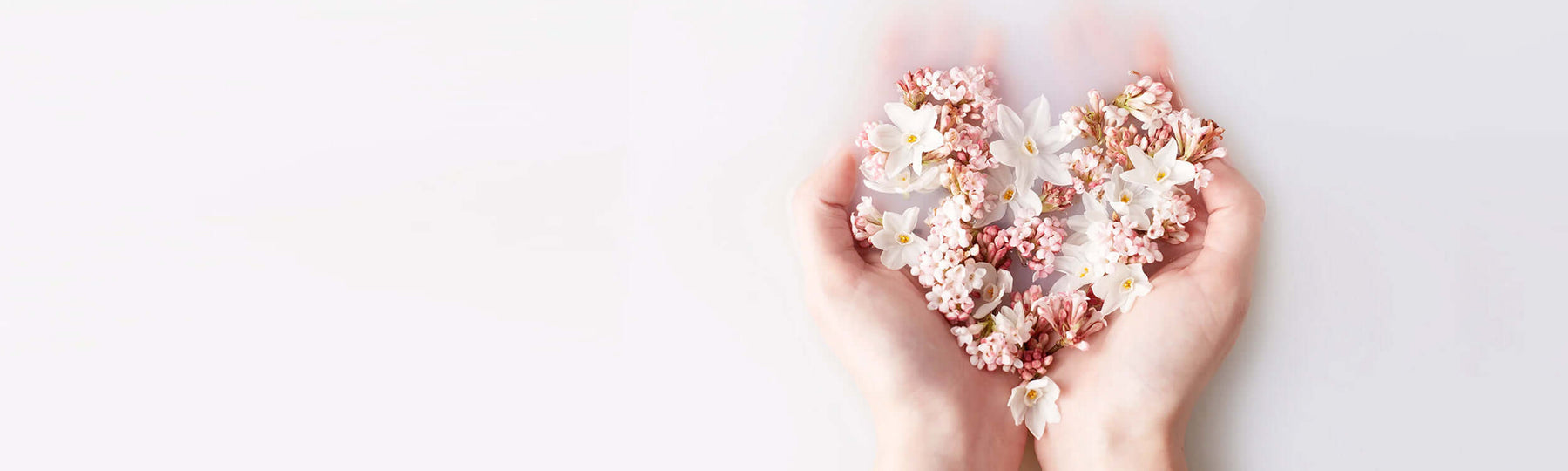 Woman dipping her hands in a milky bath, holding flower petals shaping a heart form by Neal's Yard Remedies