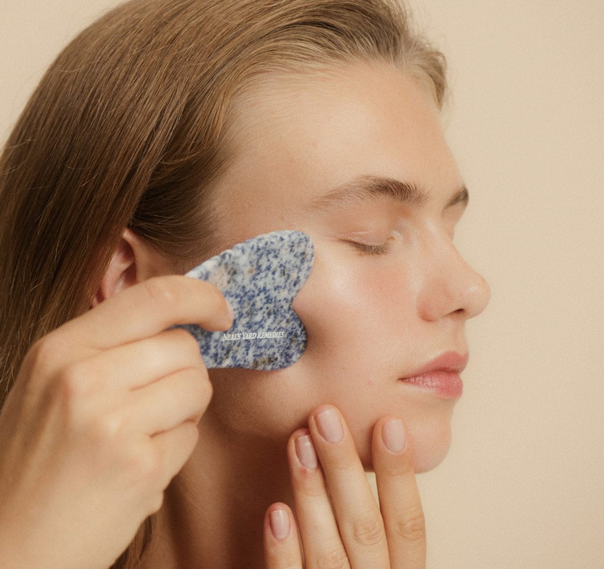 Person applying a blue floral face mask to their face against a beige background
