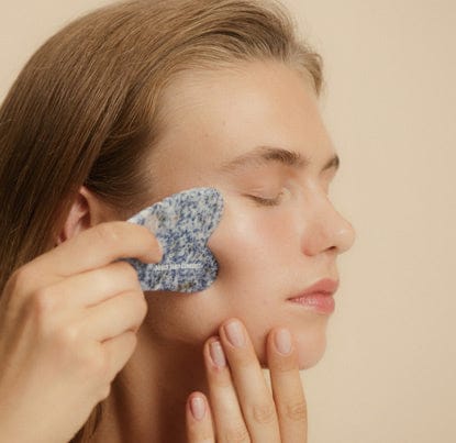 Person using a blue facial scrubber on their face against a beige background